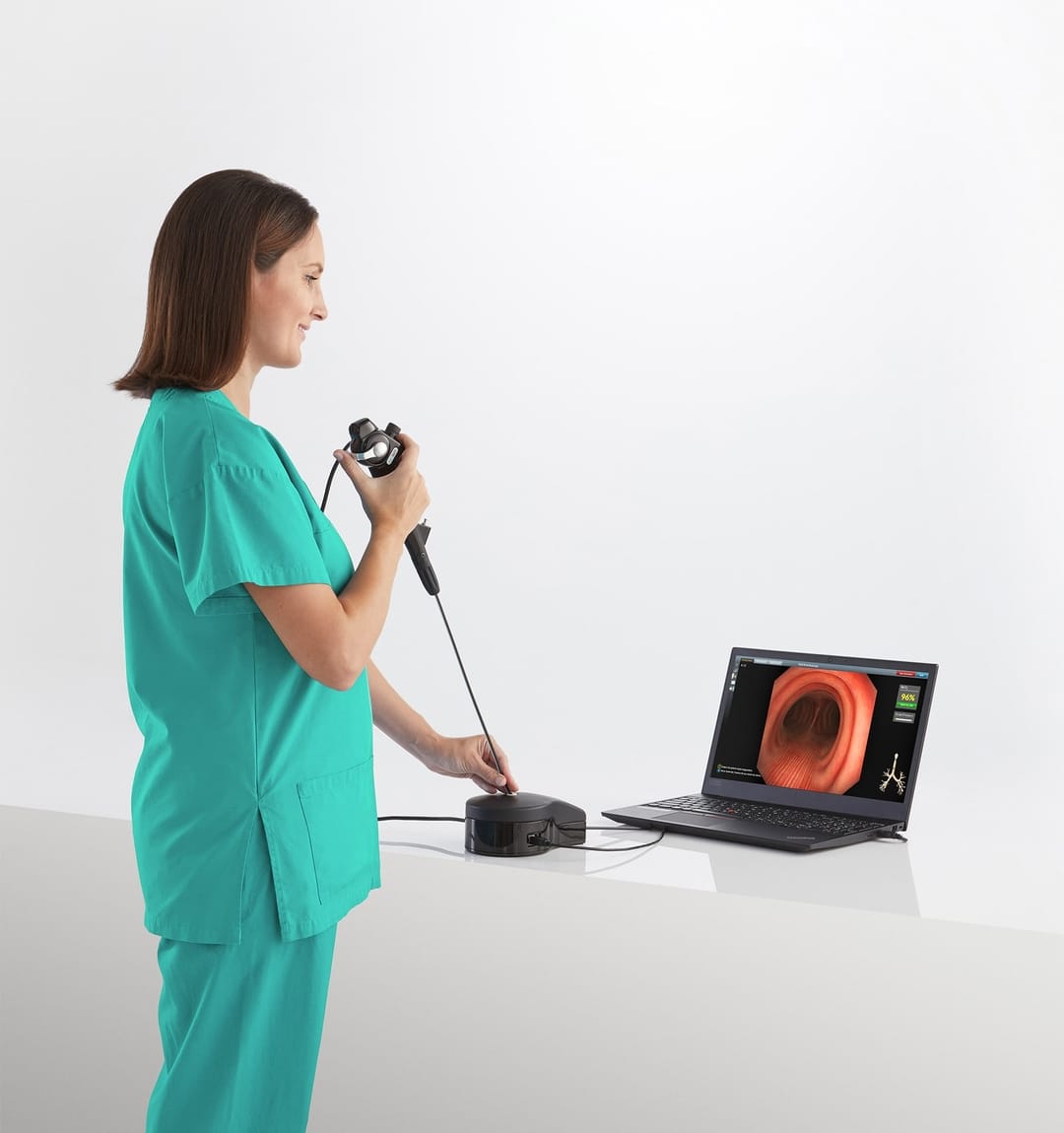 A medical professional in scrubs using an endoscopy training simulator while looking at a monitor.