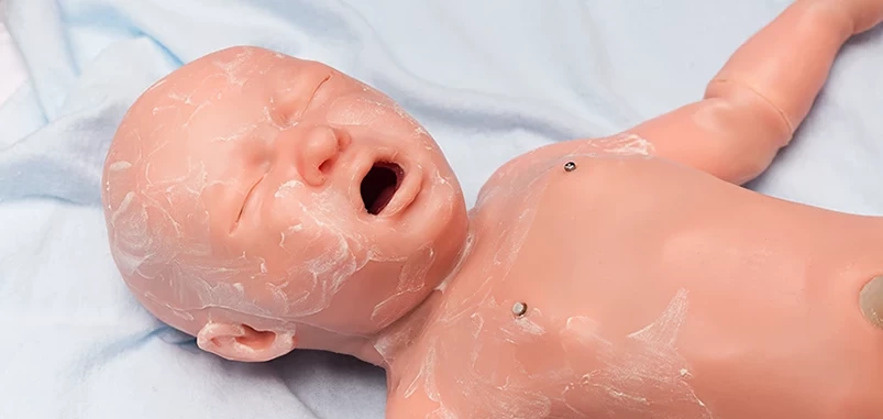 A close-up of a lifelike medical training mannequin resembling a newborn baby, with its mouth slightly open as if crying.